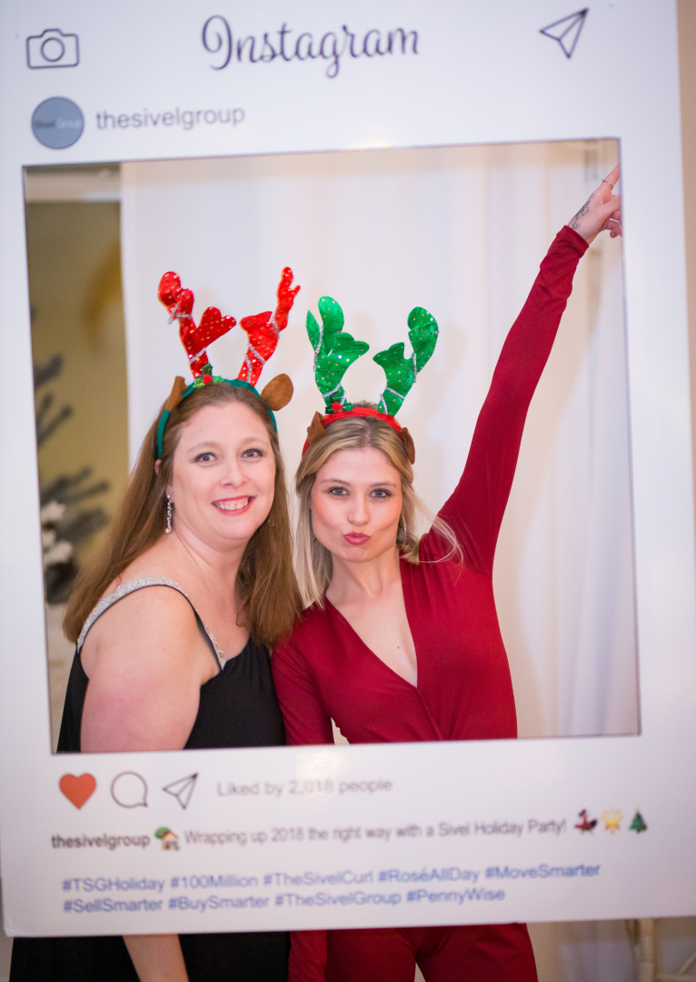 Guests pose in a large frame at an office holiday party in the Loft 