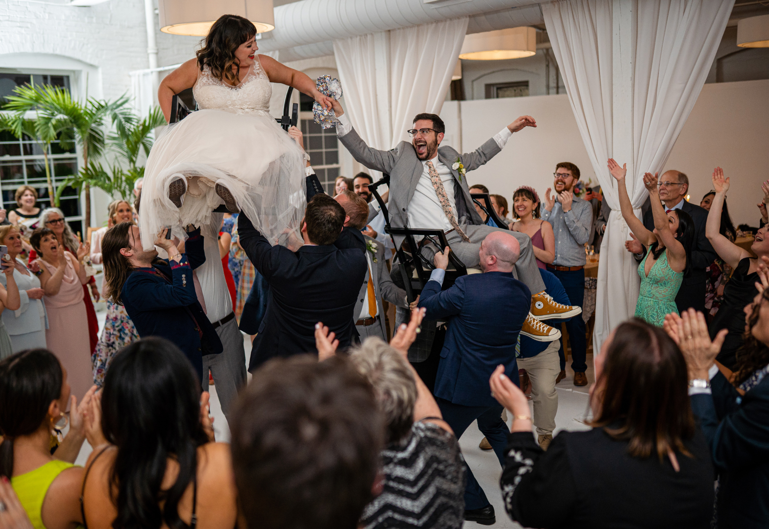 Guests dancing and holding up the bride and groom in chairs at a Jewish wedding