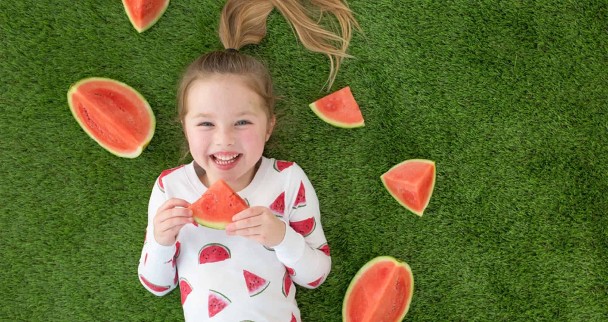 Overhead shot of young girl wearing pajamas in a watermelon print while eating watermelon