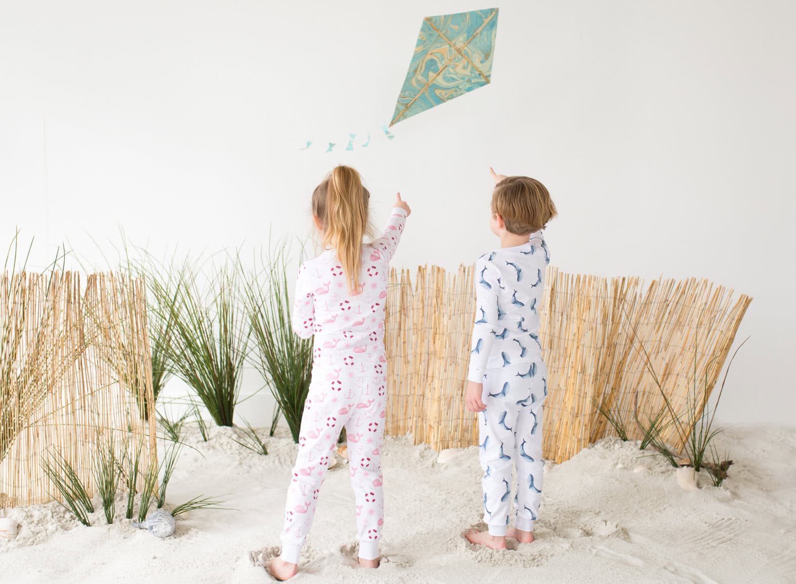 Two young children in printed pajamas flying a cute in a beach scene