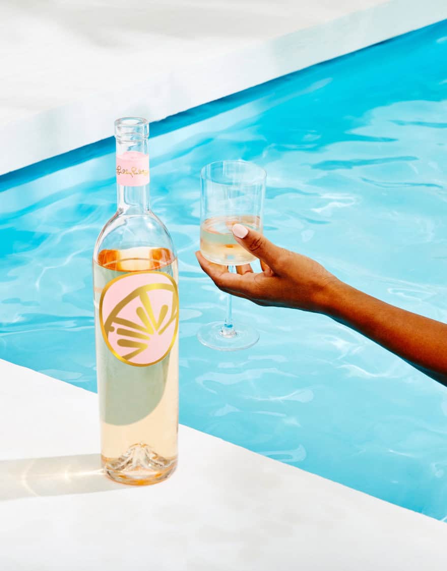 Hand holding glass of rosé on the edge of blue pool