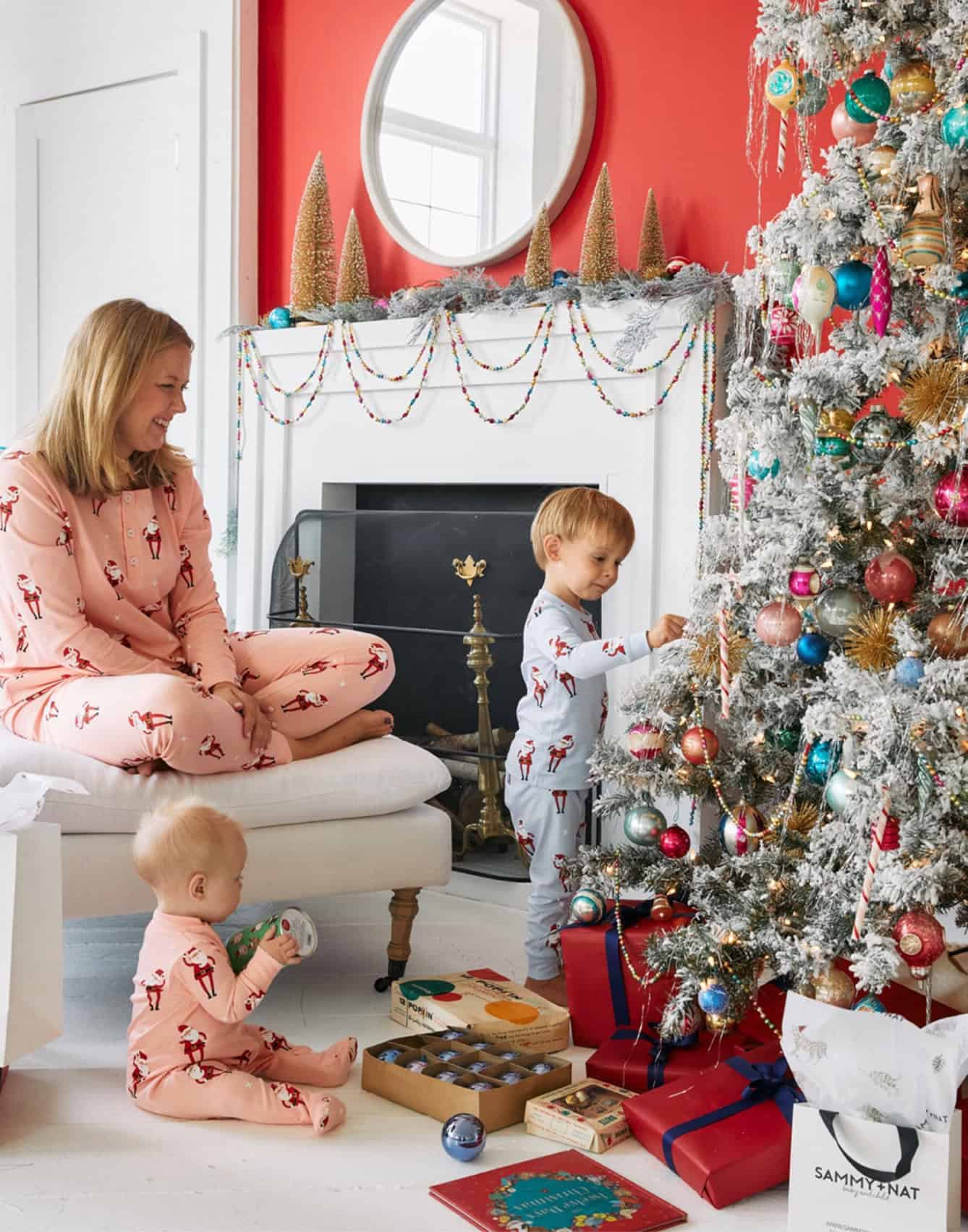 Two young children and their mother in printed pajamas in a living room set decorated for Christmas