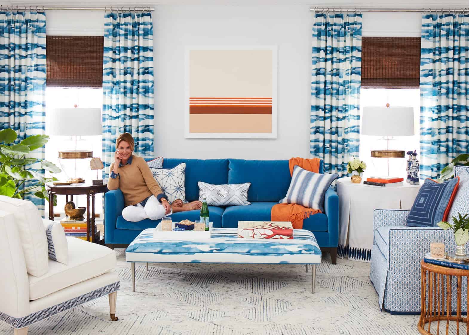 Living room set in blues with pops of orange and female model sitting on sofa