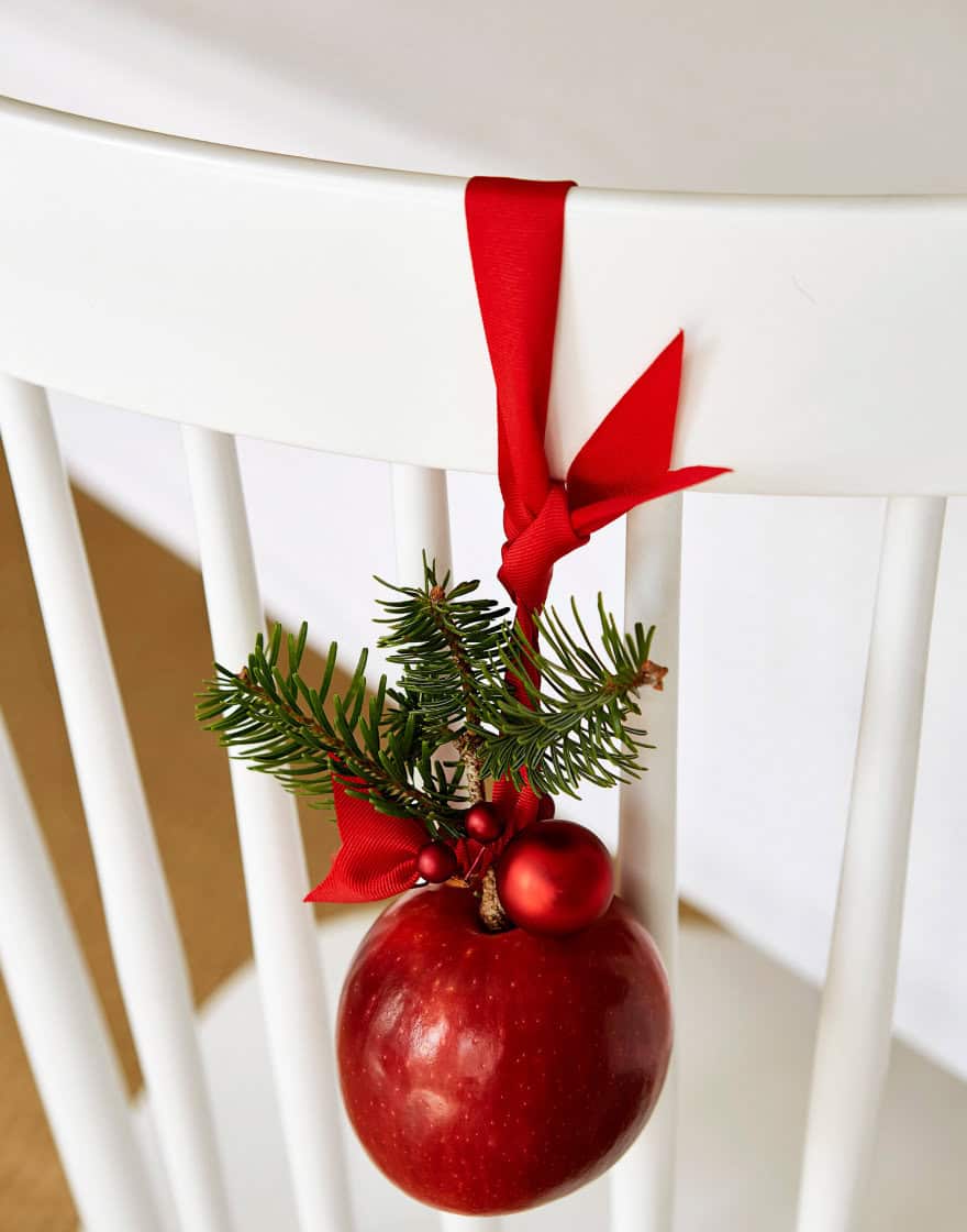 Apple, greenery and ribbon embelling the back of a white dining chair