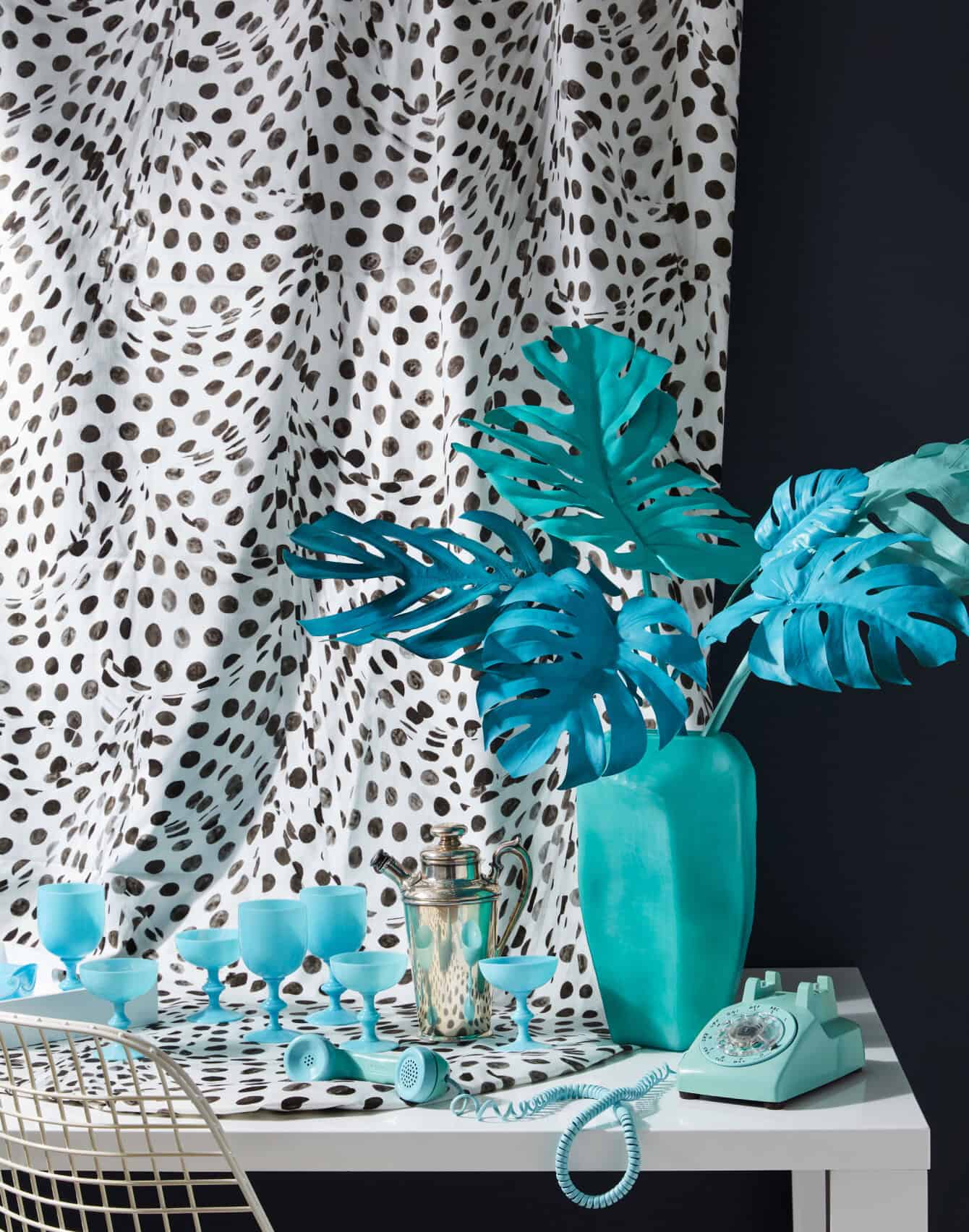 Exuberant black-and-white wallpaper behind a display of turquoise objects on a white table