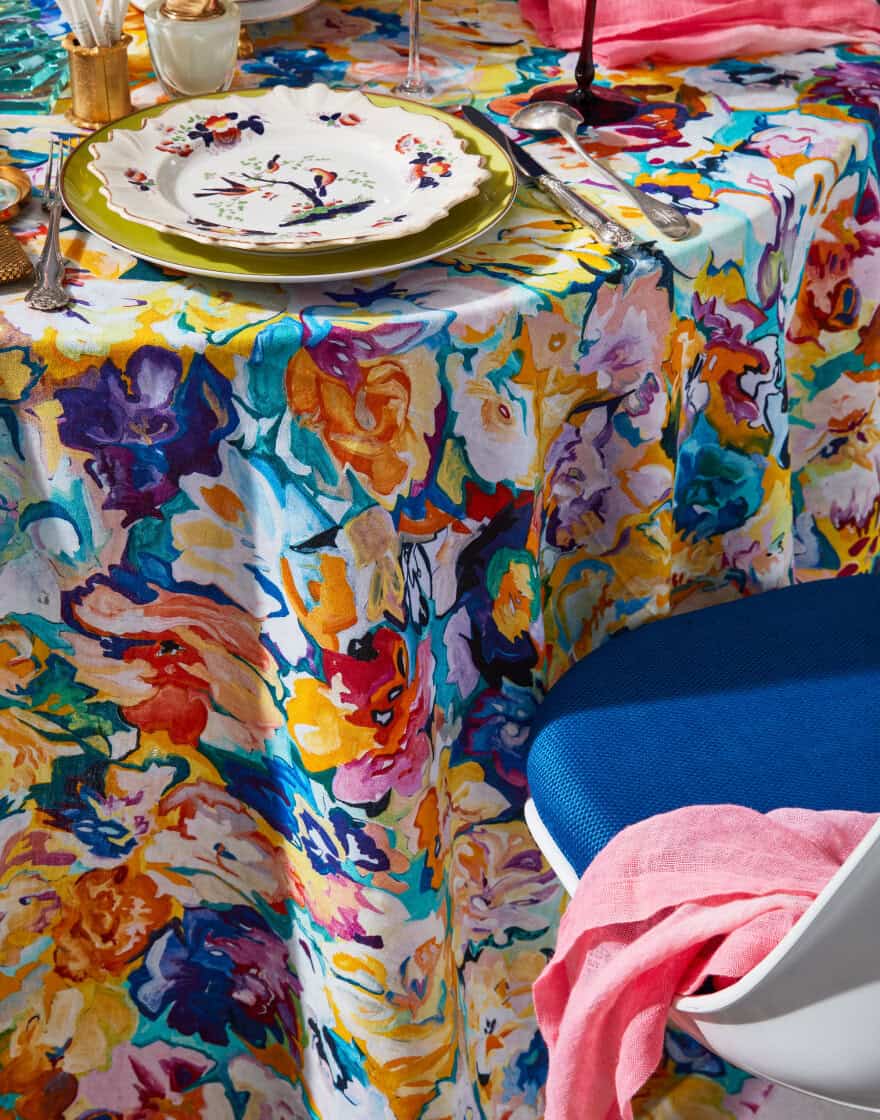 Multi-colored tablecloth with vintage tableware and mid-century modern dining chair with blue cushion