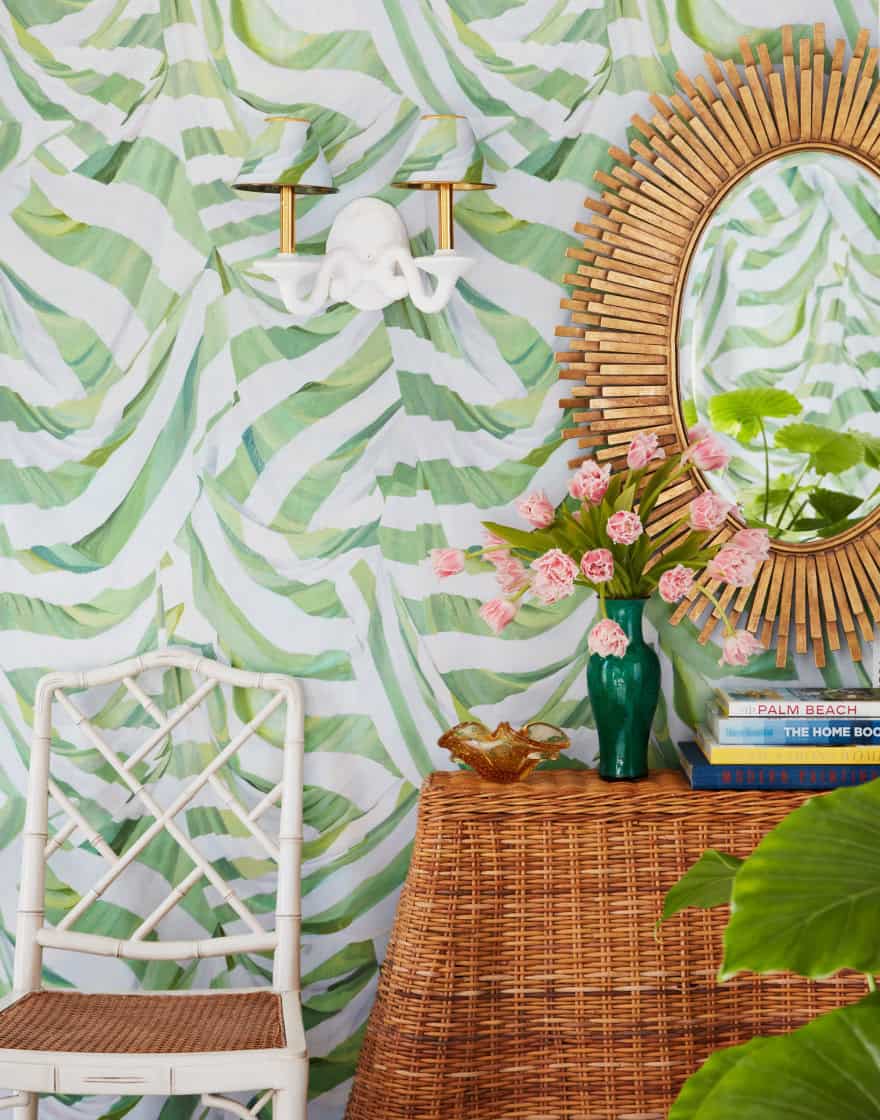 Foyer vignette with green-and-white wallpaper, sunburst mirror and rattan console table