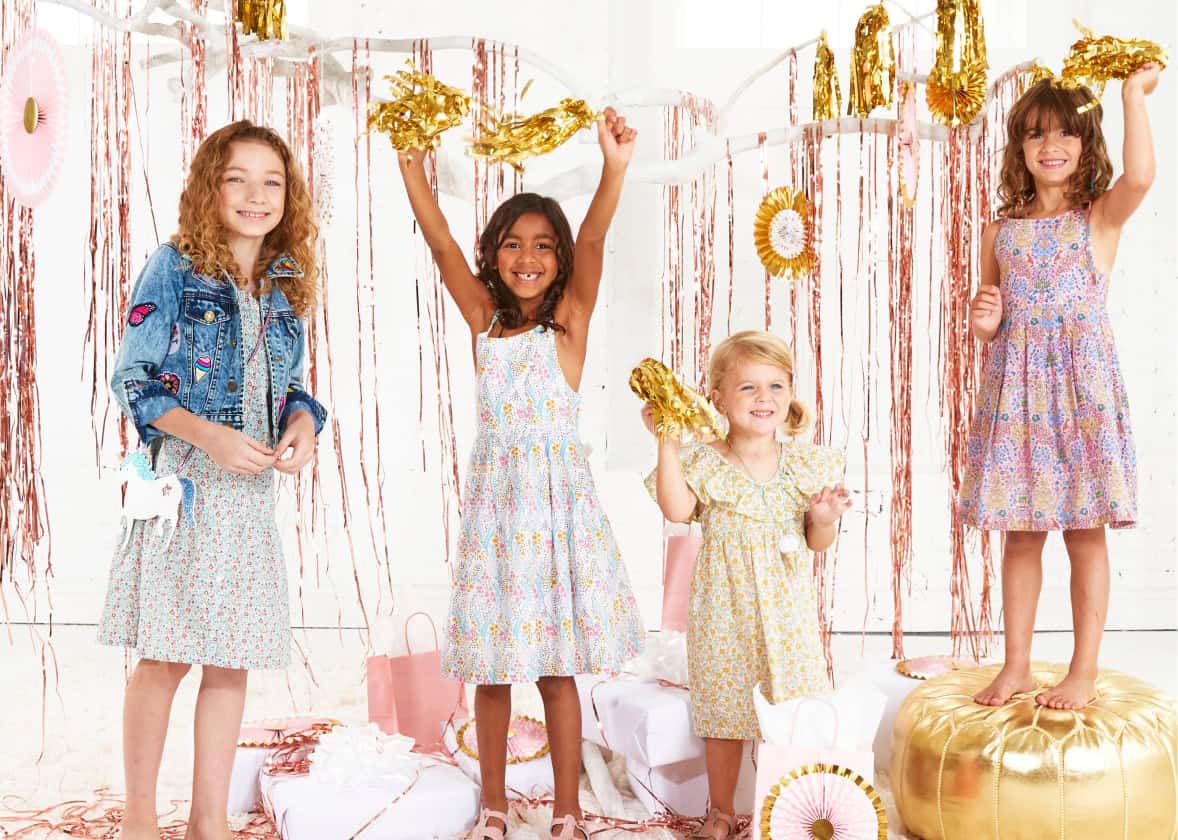 Young girls in party dresses playing beneath a white painted tree with gold streamers